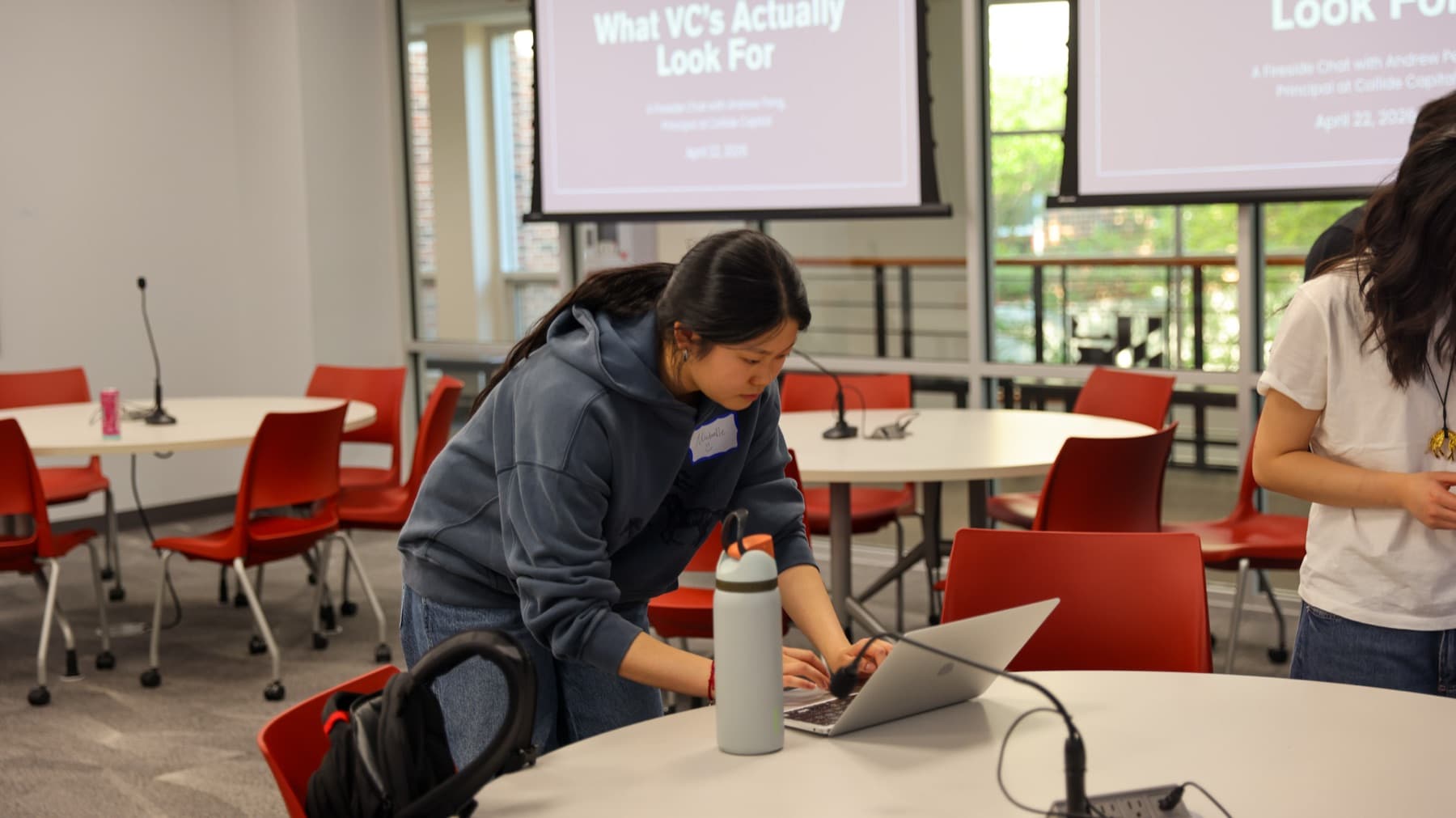 A DVCG analyst working at a laptop before a session, the day's title slide on the screens behind